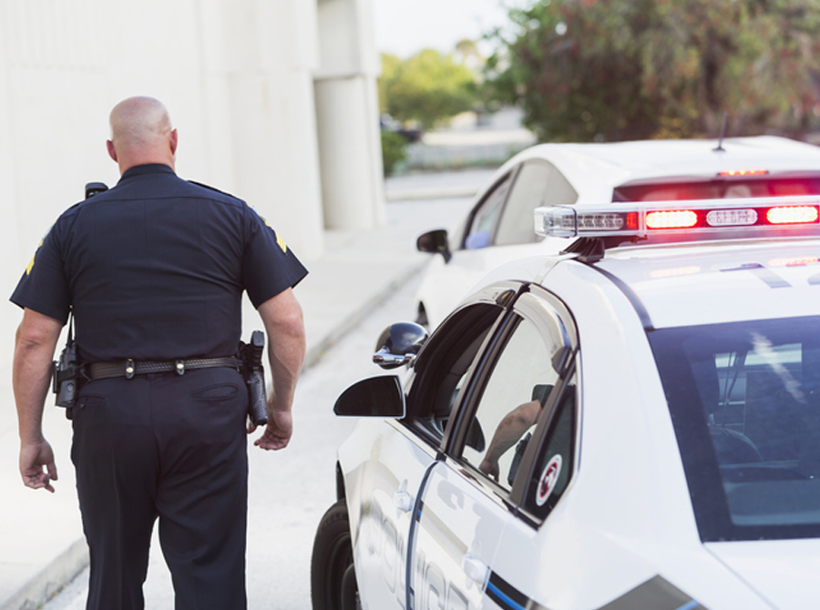 A police officer walks alongside a police car on the street, maintaining a visible presence for community security.