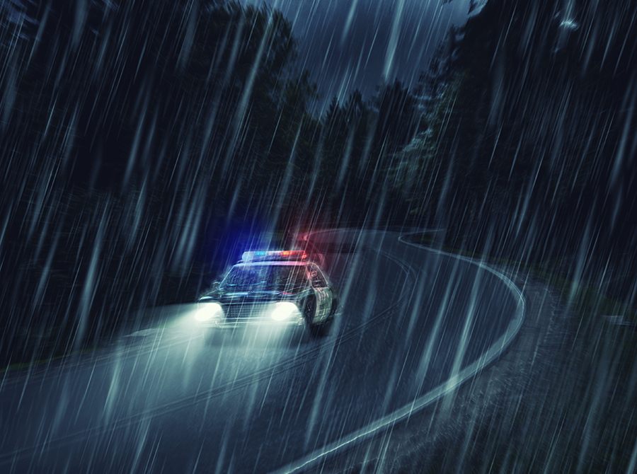 A police car moves along a rainy road at night, with raindrops glistening on the surface and lights aglow.