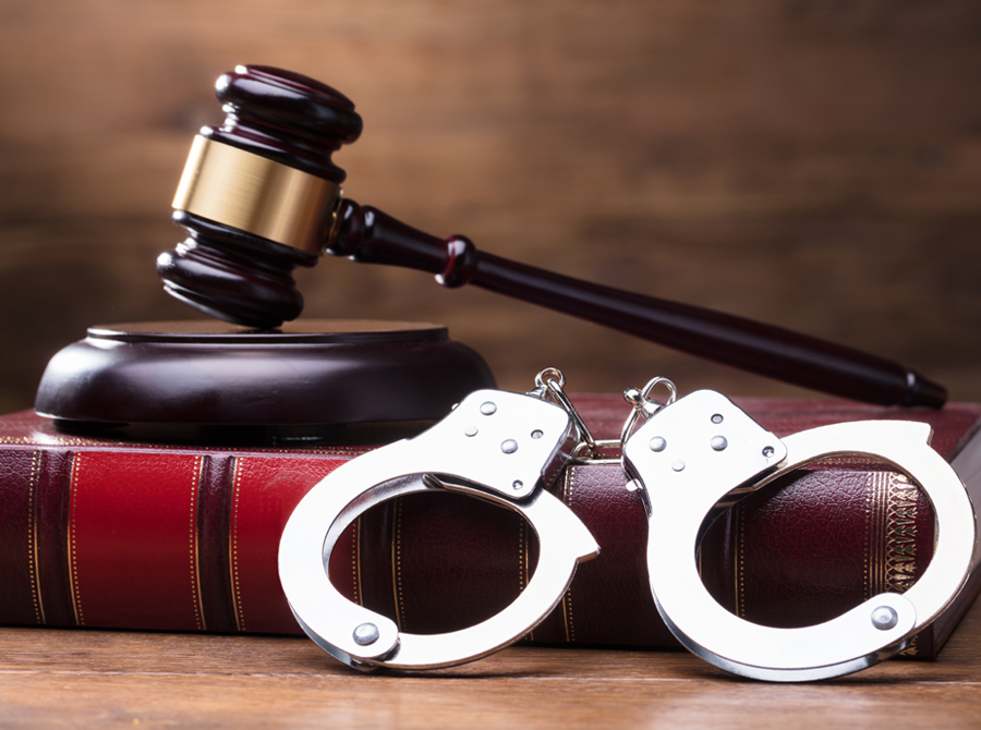 A gavel and handcuffs placed on a book, symbolizing law and justice.