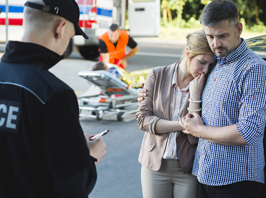 A police officer documents the scene of an emergency while comforting civilians in distress, symbolizing the importance of verbal de-escalation techniques in law enforcement training.