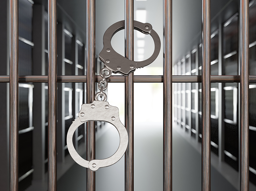 Handcuffs hang on the bars of a dimly lit prison cell, reflecting Restraint Chair Use & Constitutional Rights as the corridor stretches into the background with a sense of confinement and isolation.