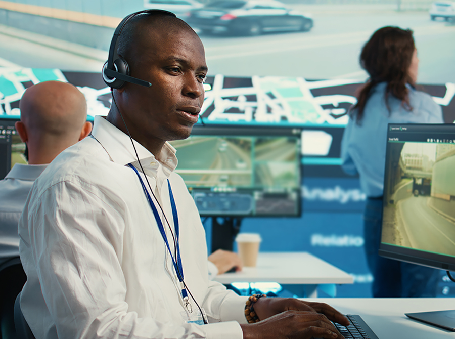 A 9-1-1 dispatcher wearing a headset works at a computer in a high-tech emergency center, illustrating the reality of 9-1-1 dispatch.