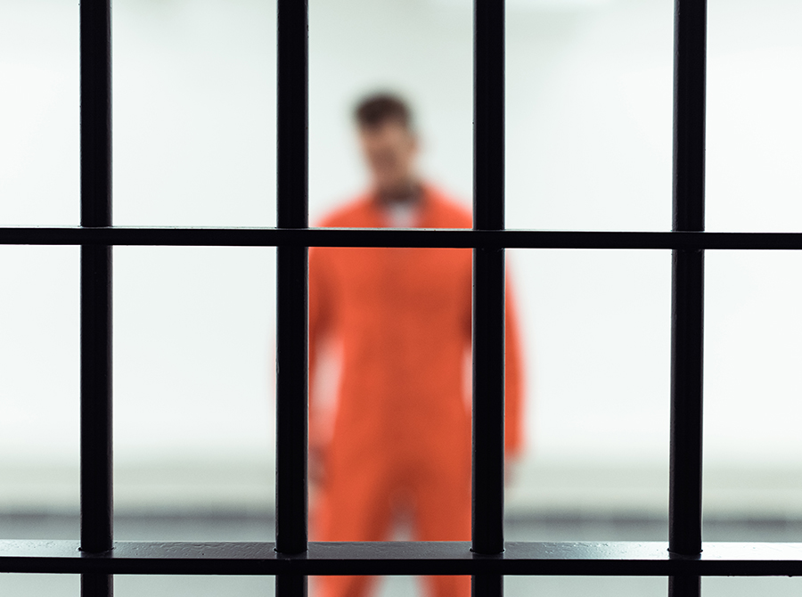 Person in an orange jumpsuit standing behind jail bars, illustrating Personality Disorders in Corrections and mental health in a correctional setting.
